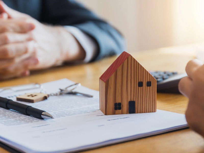 Small house figure on a desk with a document, pen, and calculator. This image accompanies the page titled Estate Planning Services in Cary.