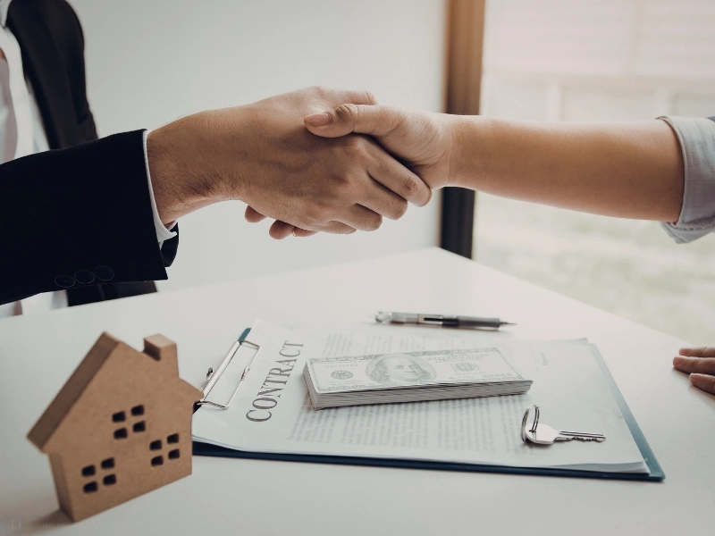 A Wake Forest estate administration attorney shakes hands with a client after signing documents on a desk with cash.